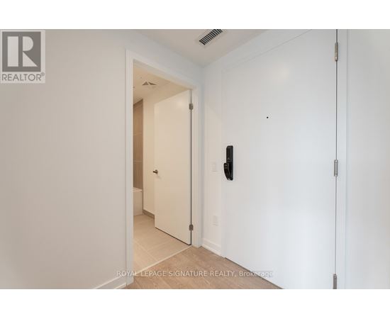 A white hallway with a door on the left and a wall-mounted light switch on the right.