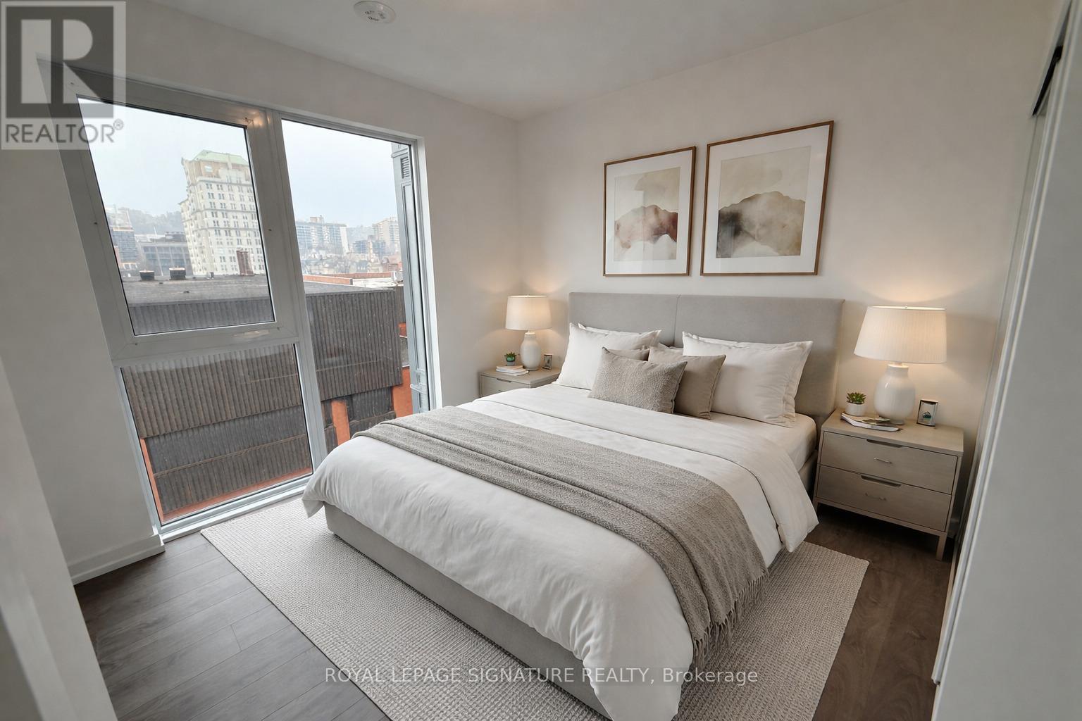 A bedroom with a large bed, two nightstands with lamps, and a view of the city through a large window.
