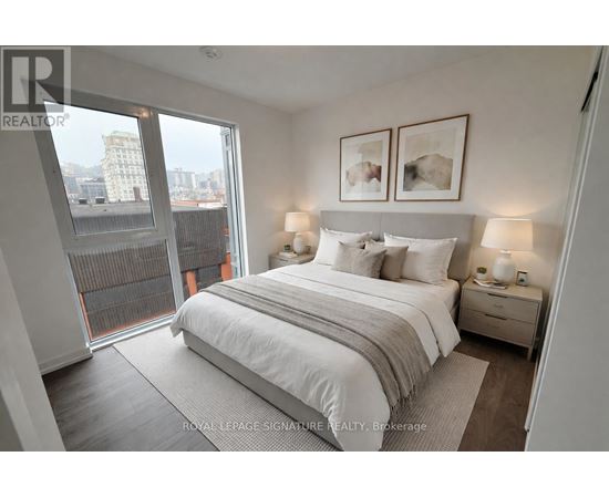 A bedroom with a large bed, two nightstands with lamps, and a view of the city through a large window.