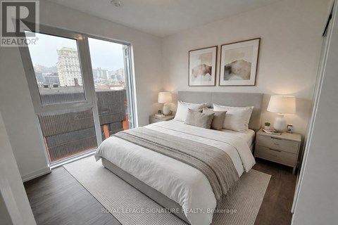 A bedroom with a large bed, two nightstands with lamps, and a view of the city through a large window.