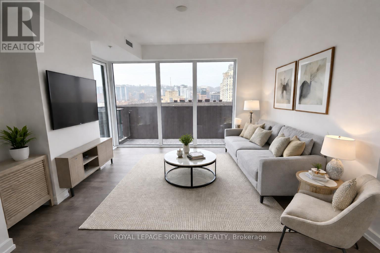 A living room with a flat screen TV, a sofa, a coffee table, and a large window with a view of the city.