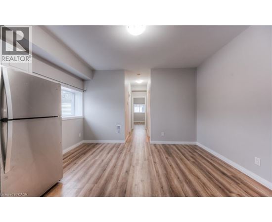 A spacious room with wooden flooring and a refrigerator on the left side.
