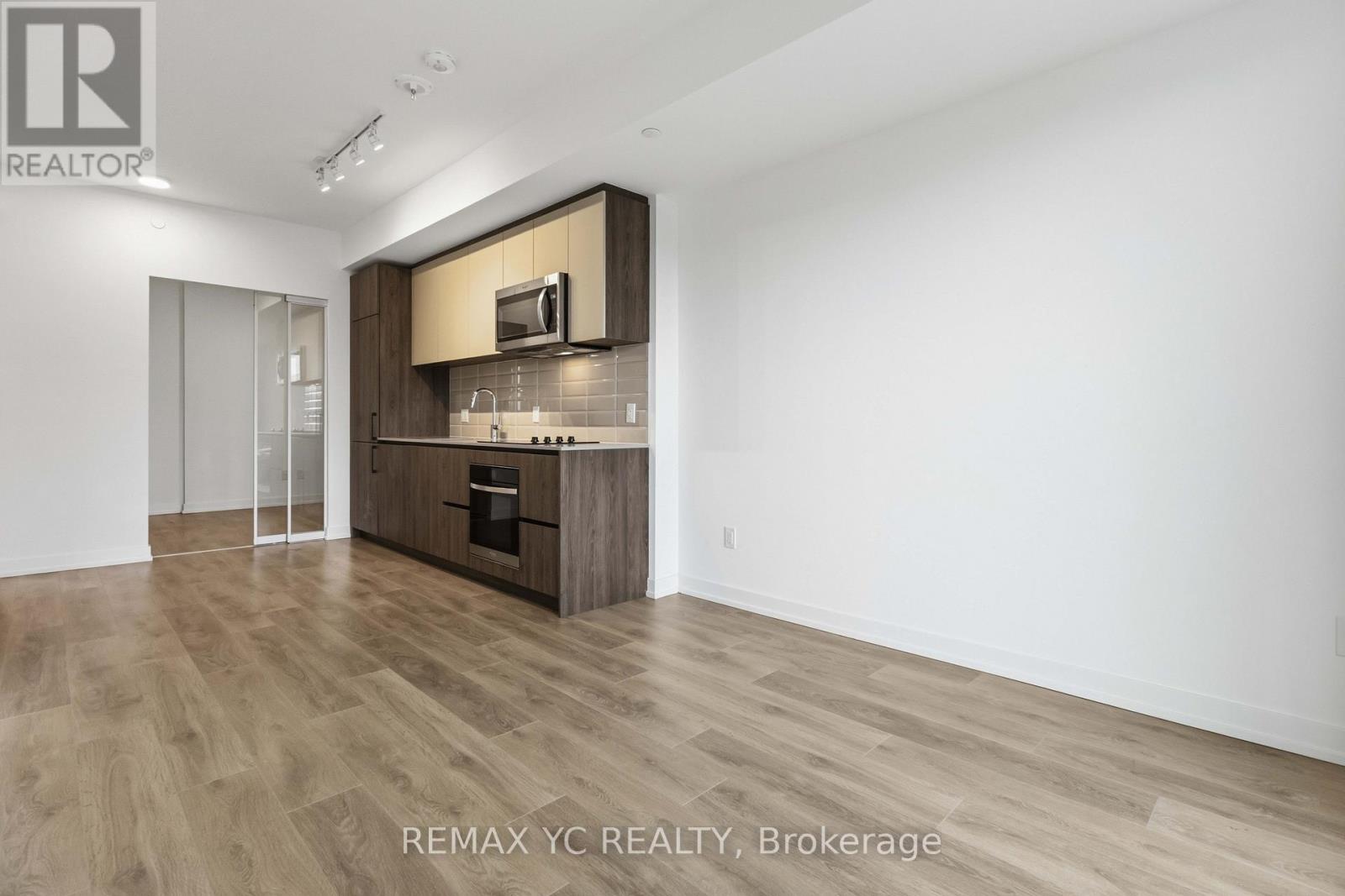 A spacious, empty room with wood flooring and a kitchenette area.