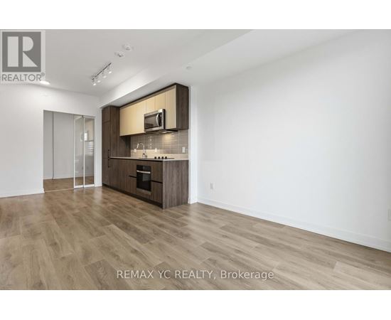 A spacious, empty room with wood flooring and a kitchenette area.