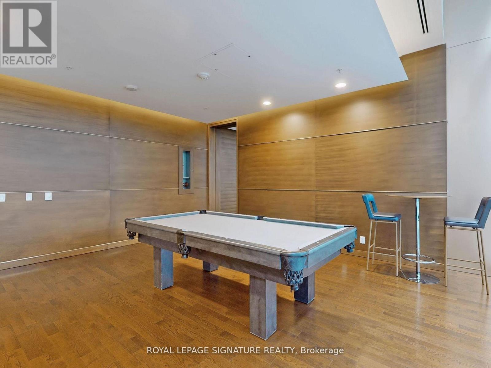 A pool table in a room with wood paneling and a bar stool.