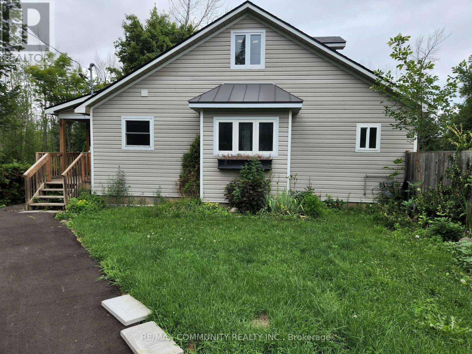 A house with a grey siding and a brown roof with a small porch and a small garden in front.