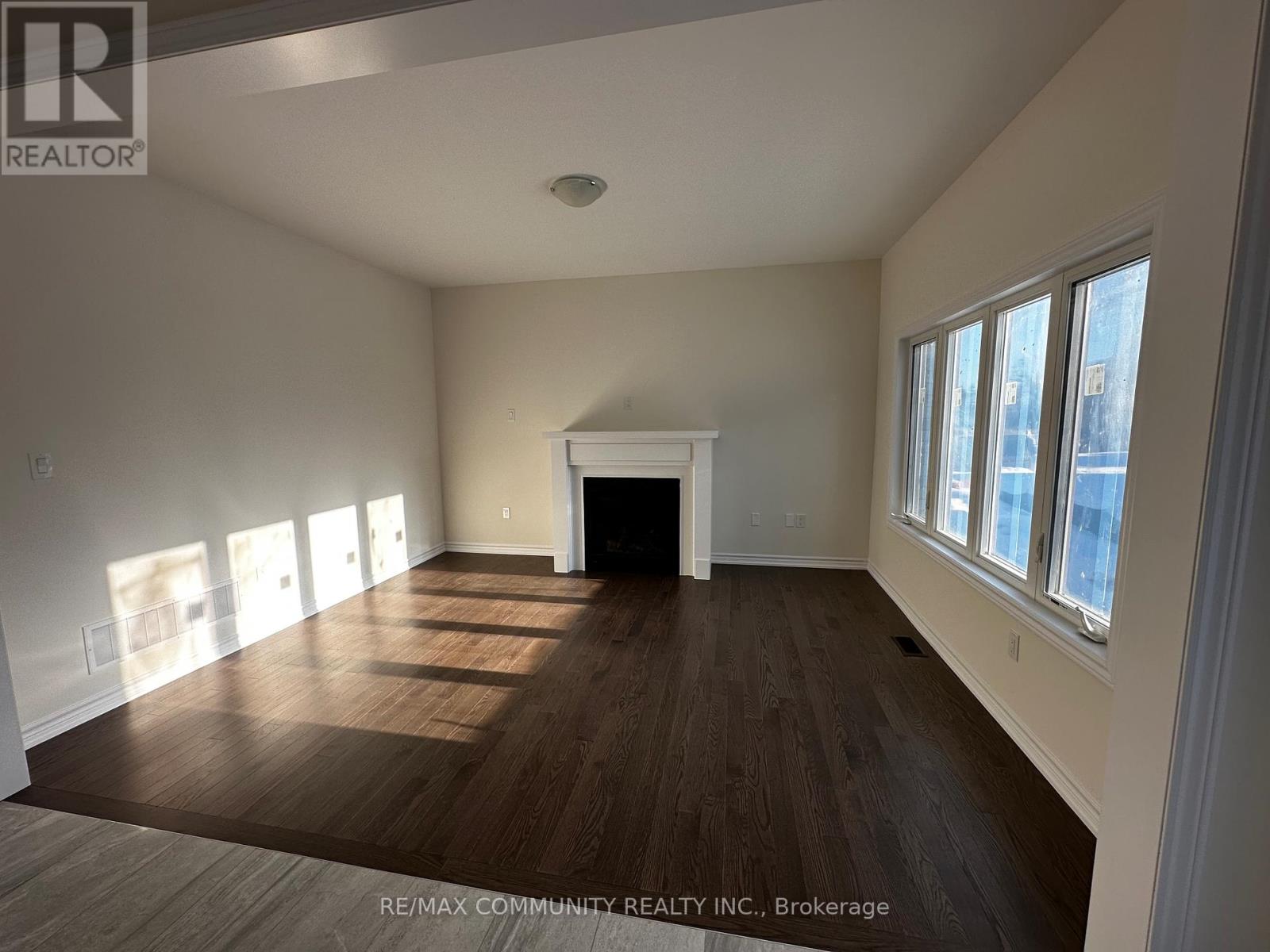 A large, empty room with wood flooring and a fireplace.