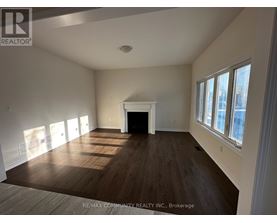 A large, empty room with wood flooring and a fireplace.