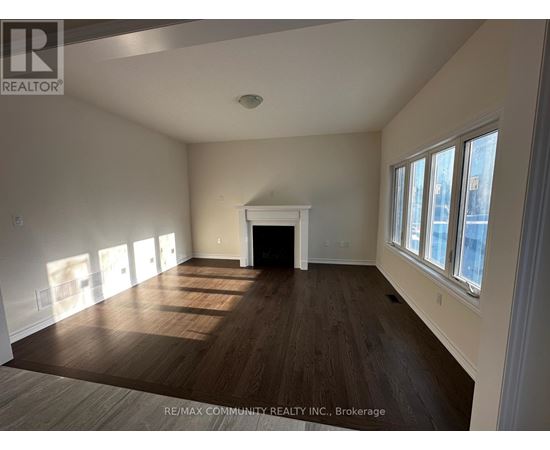 A large, empty room with wood flooring and a fireplace.