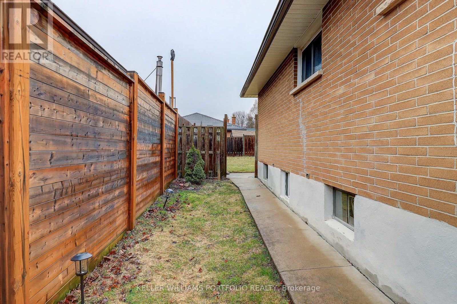 A wooden fence runs along the side of a brick house.