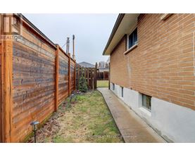A wooden fence runs along the side of a brick house.