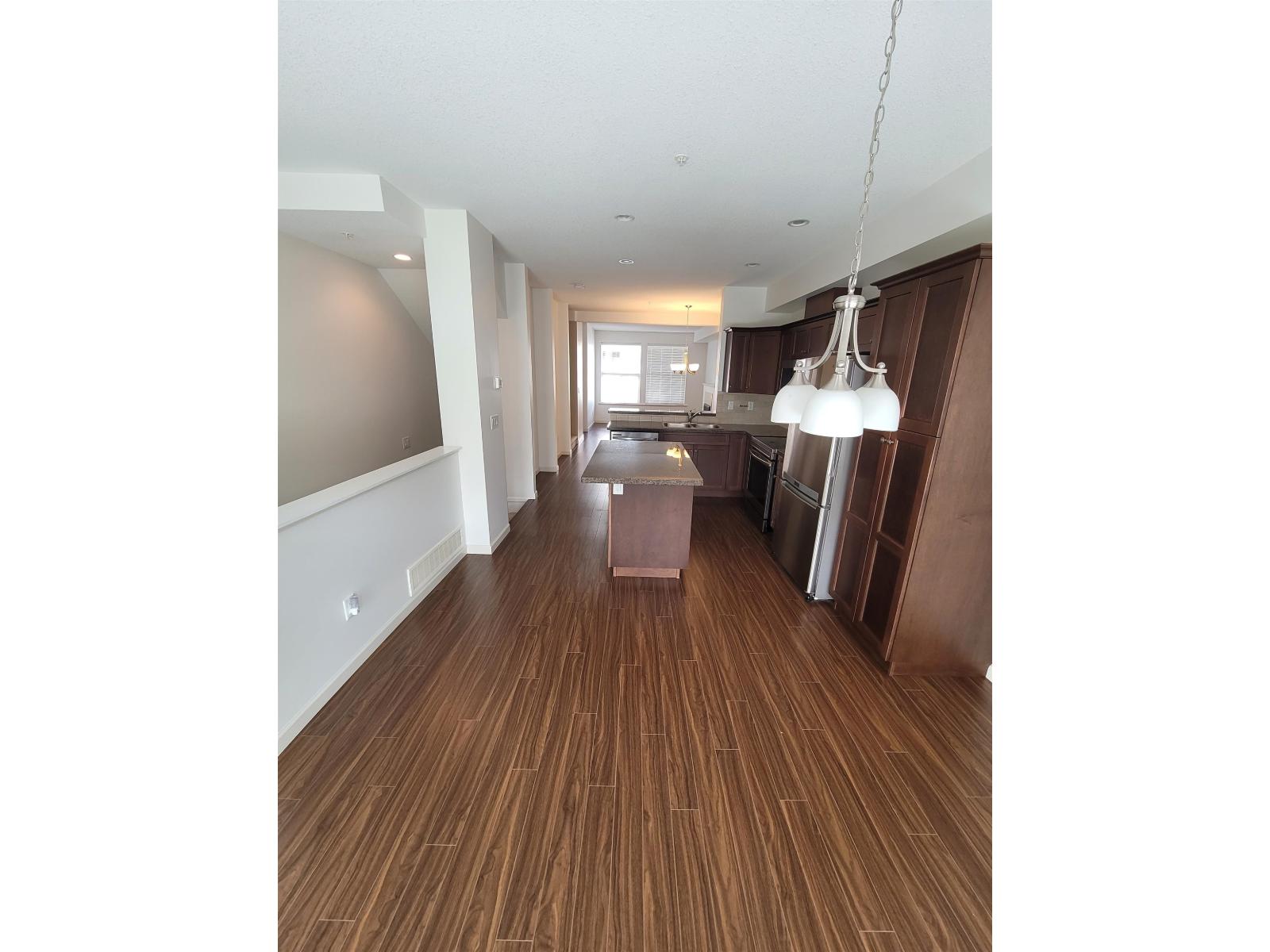 A long hallway with a brown floor and a chandelier hanging from the ceiling.