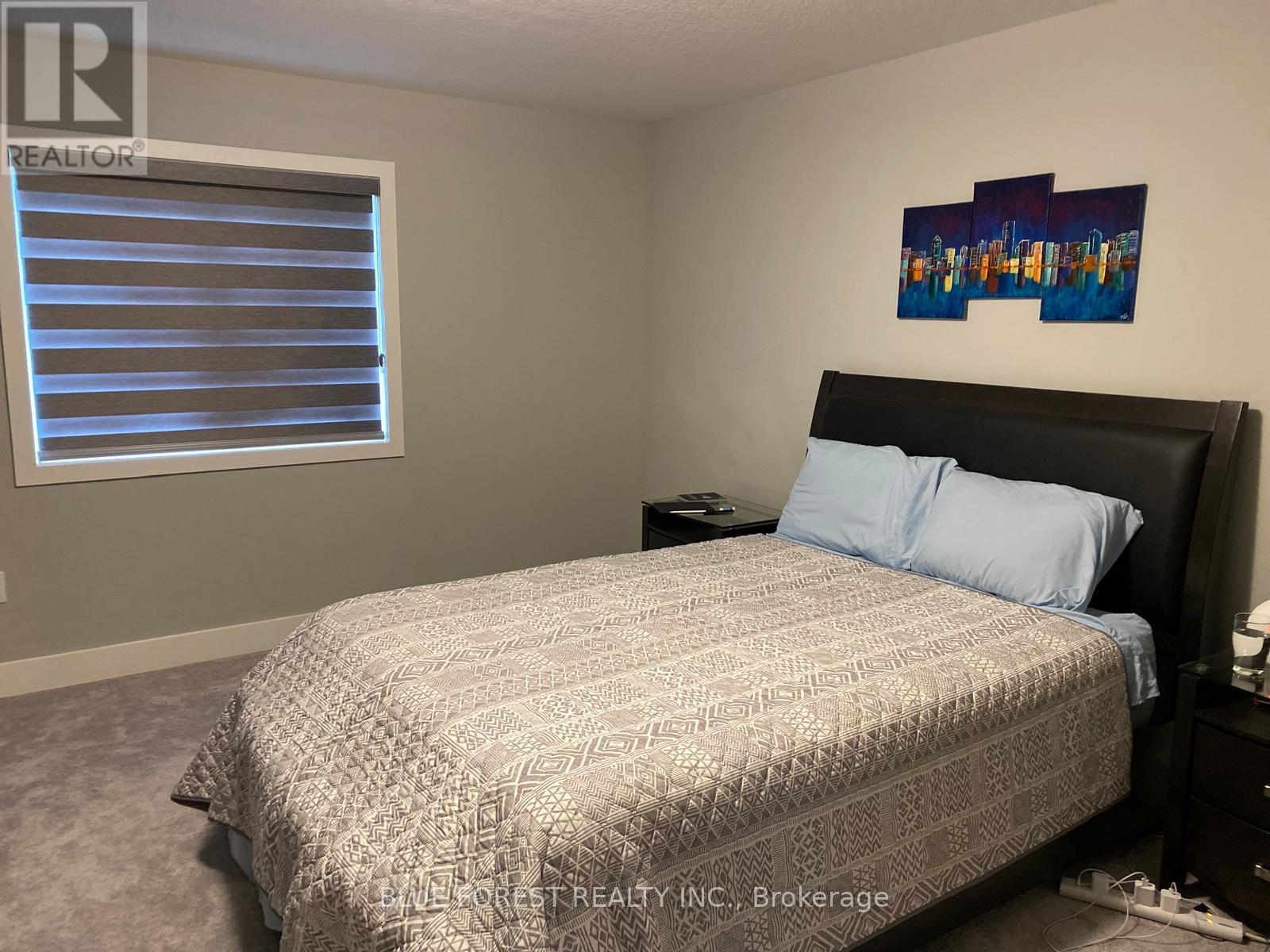 A bedroom with a bed, nightstand, and window with blinds.
