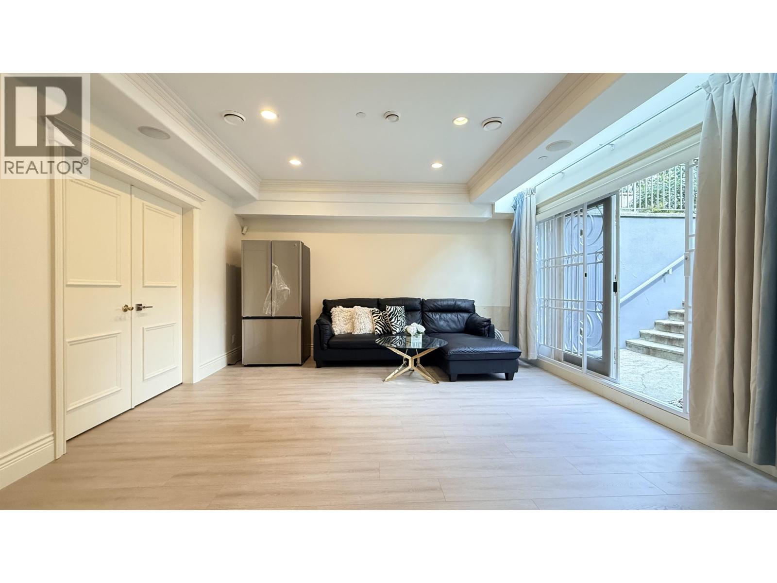 A spacious living room with a black sofa and a wooden floor.