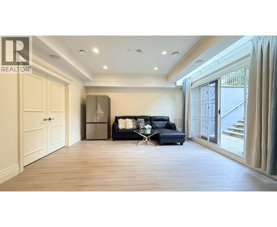 A spacious living room with a black sofa and a wooden floor.