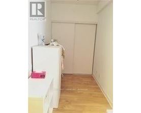 A white refrigerator sits in a kitchen with a white wall and wooden floor.