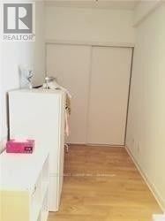 A white refrigerator sits in a kitchen with a white wall and wooden floor.