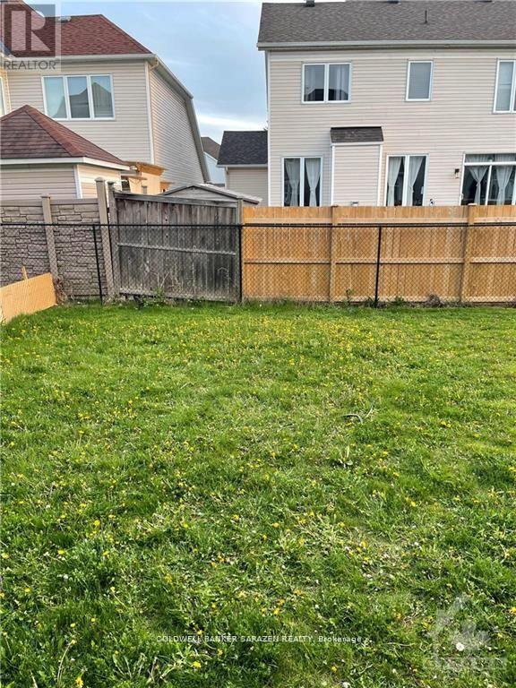 A grassy yard with a wooden fence and two houses in the background.
