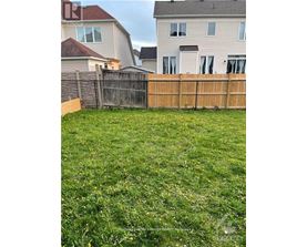 A grassy yard with a wooden fence and two houses in the background.