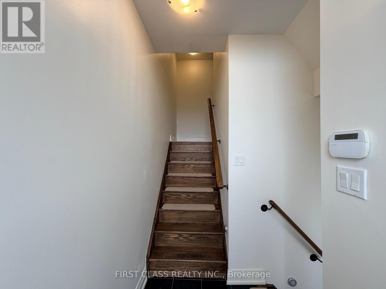 A staircase with a wooden handrail and a wall-mounted thermostat.