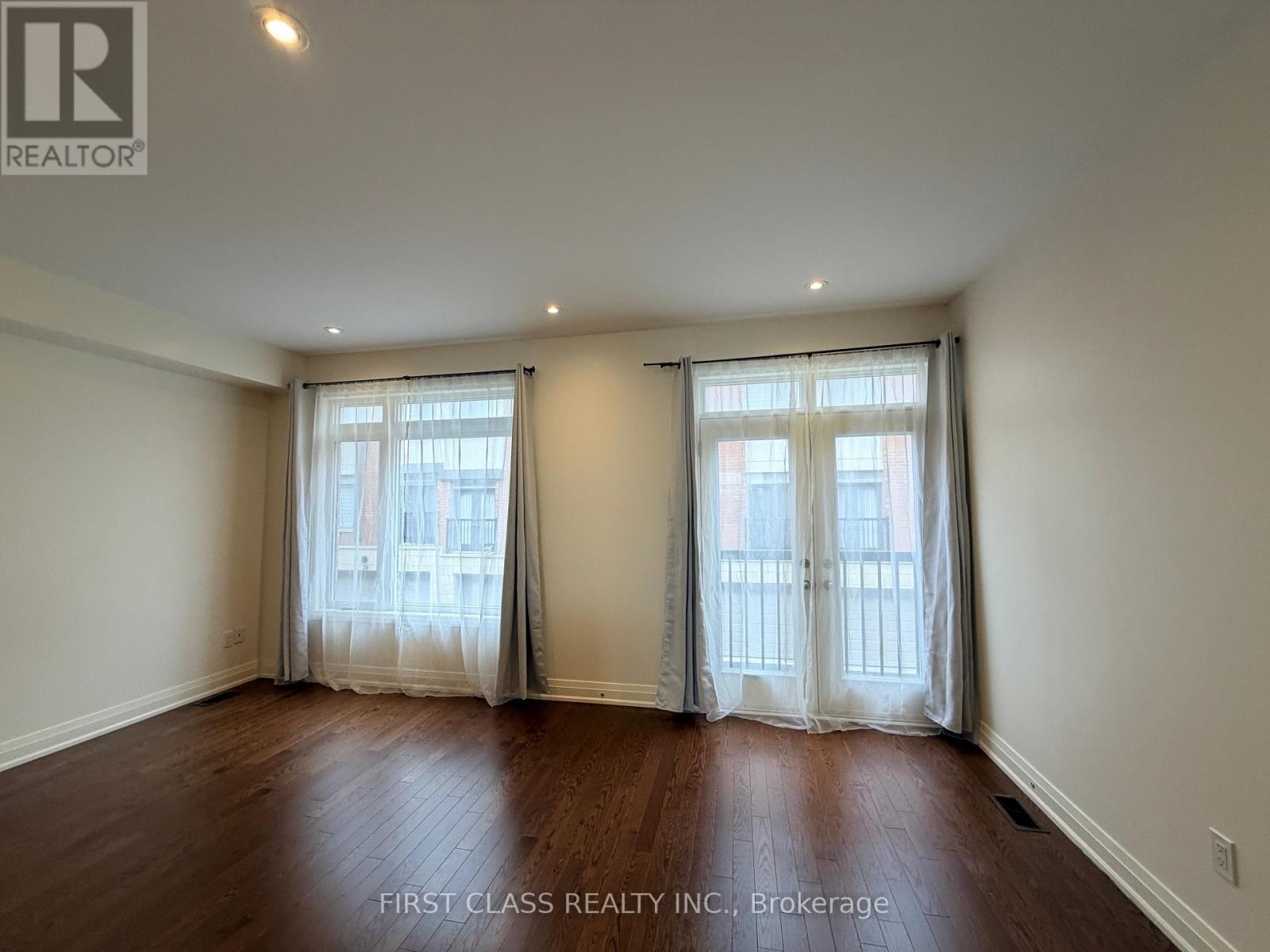 A room with wooden floors and two windows with curtains.