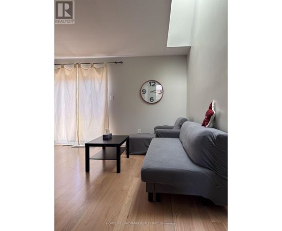 A living room with a grey couch, a black coffee table, and a clock on the wall.