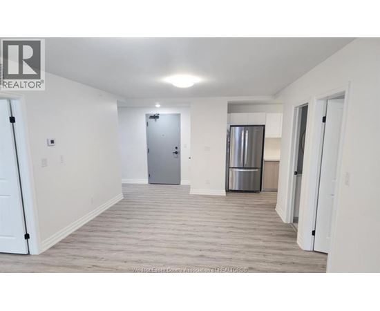 A spacious room with a door and a refrigerator in the background.