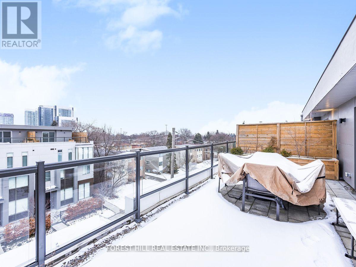 A snow-covered balcony with a hot tub and a building in the background.