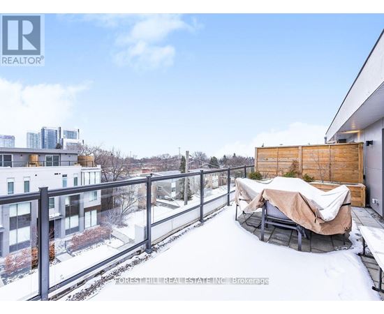 A snow-covered balcony with a hot tub and a building in the background.