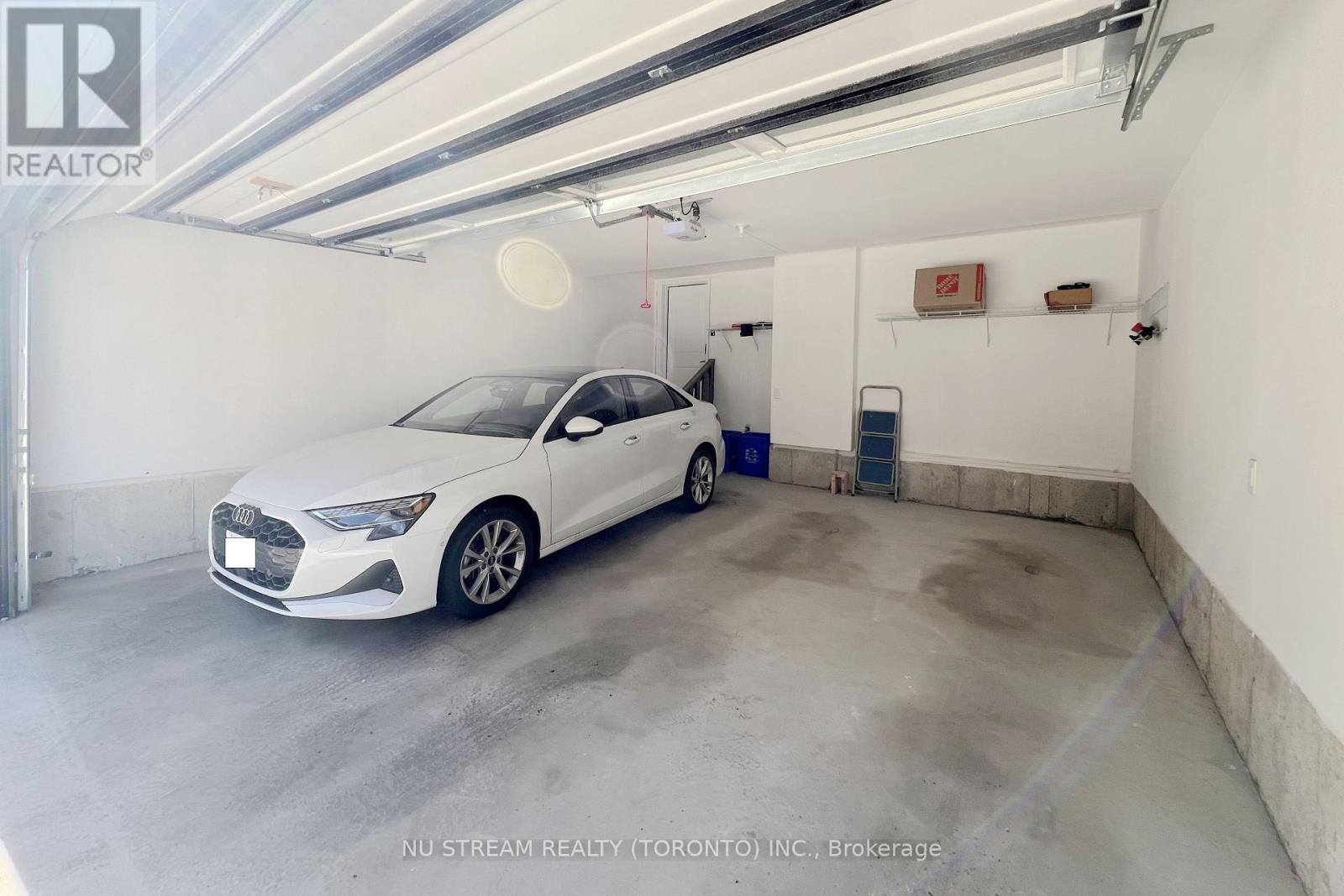 A white car is parked in a garage with a sign that reads "NU STREAM REALTY (TORONTO) INC., Brokerage.".