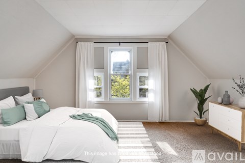 A bedroom with a large bed and a window with white curtains.