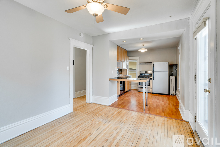 A room with a ceiling fan and a kitchen area in the background.