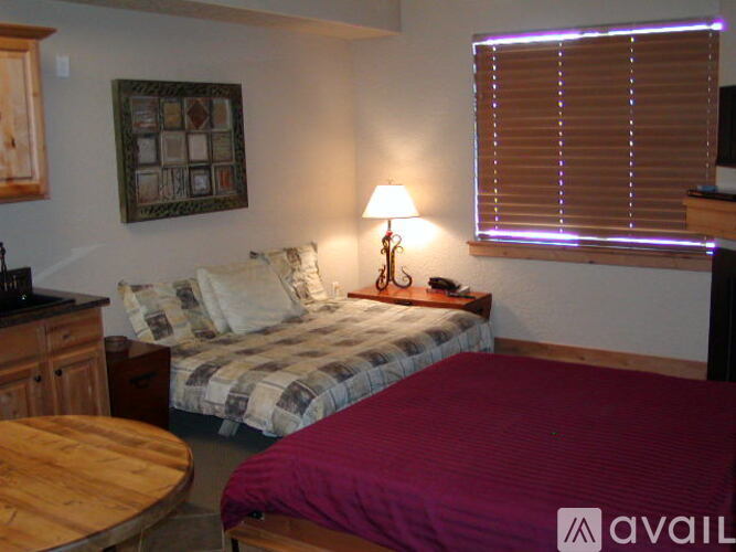 A bedroom with a bed, a table, and a window with blinds.