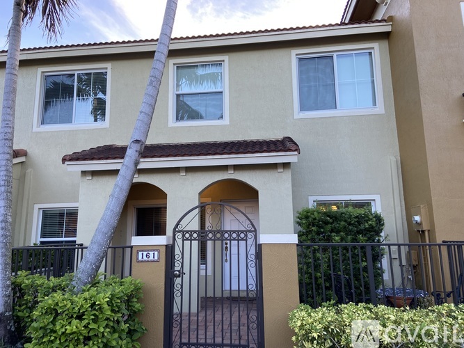 A beige house with a black gate and a palm tree in front.