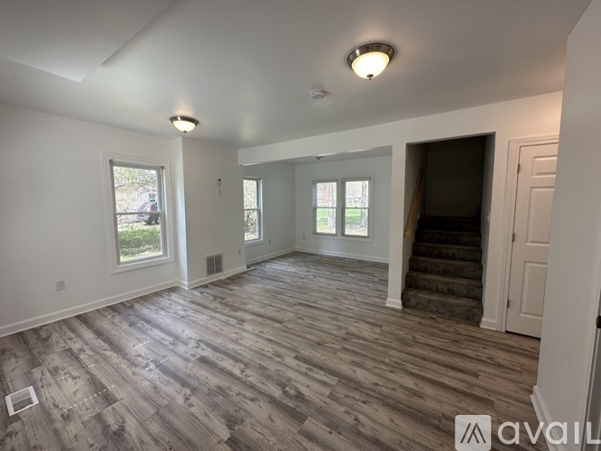 A spacious room with wooden flooring and a staircase leading to another room.