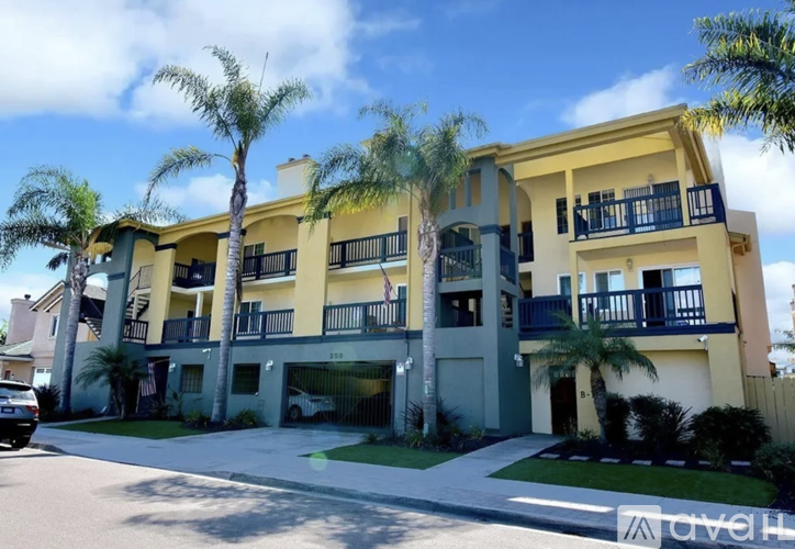 A yellow and white apartment building with palm trees in front.
