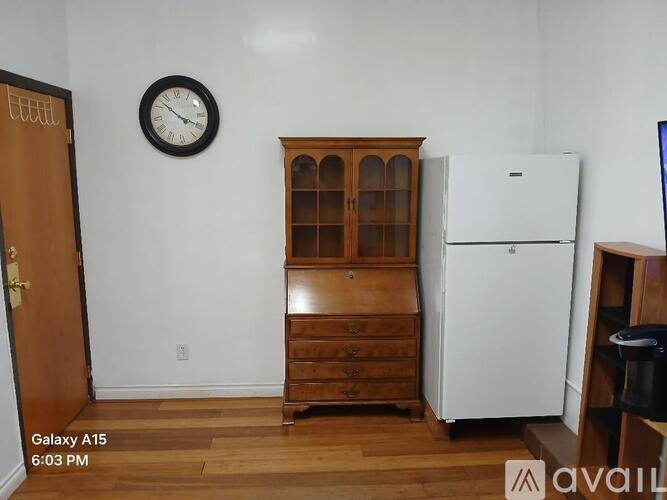 A room with a white refrigerator, a wooden cabinet, and a clock on the wall.