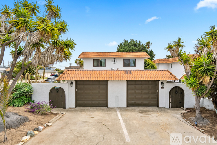 A house with a red tile roof and a garage is surrounded by palm trees.