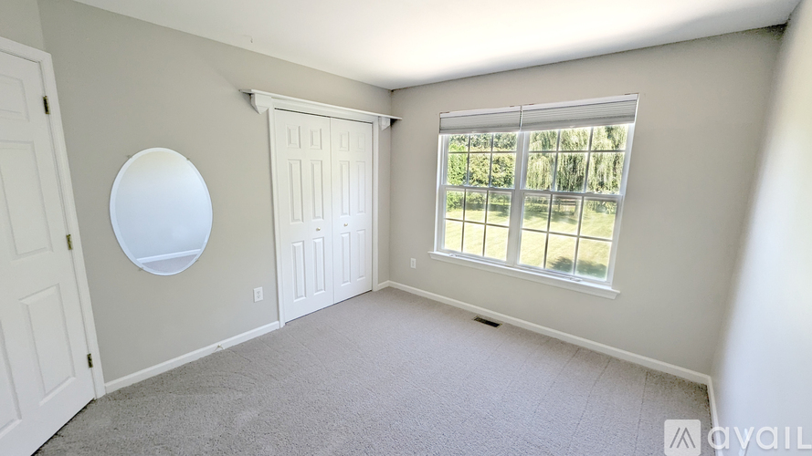 A room with a round mirror on the wall and a window with a view of trees.