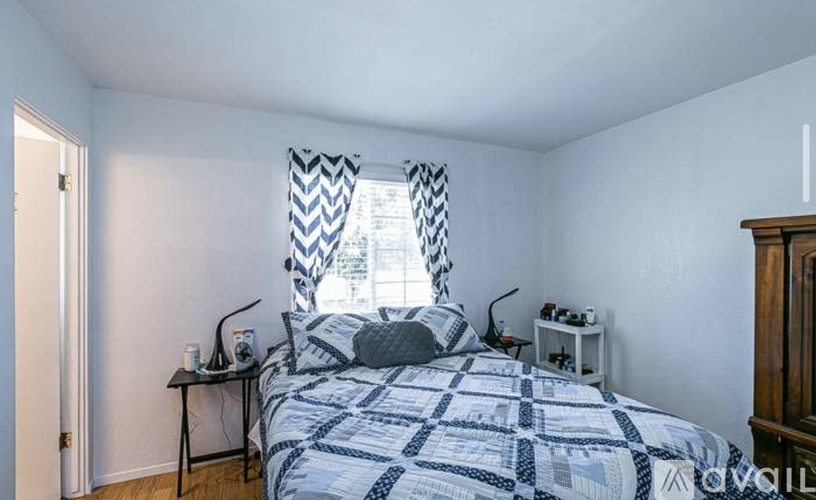 A bedroom with a bed, nightstand, and window with curtains.