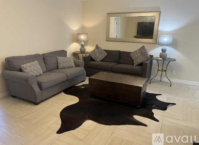 A living room with a grey couch, a brown coffee table, and a mirror on the wall.