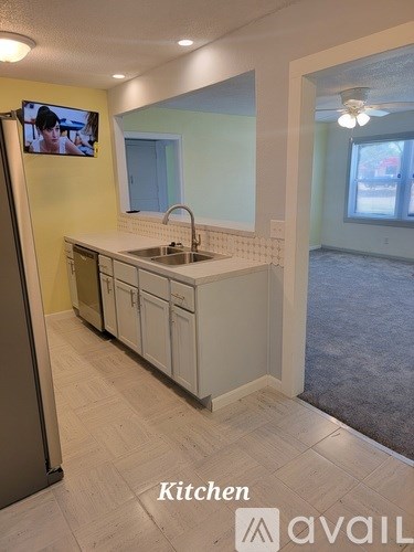 A kitchen with a sink, cabinets, and a TV mounted on the wall.
