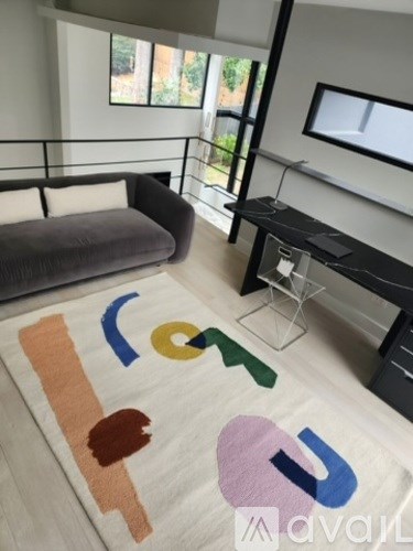 A modern living room with a grey couch and a white rug with colorful letters on it.
