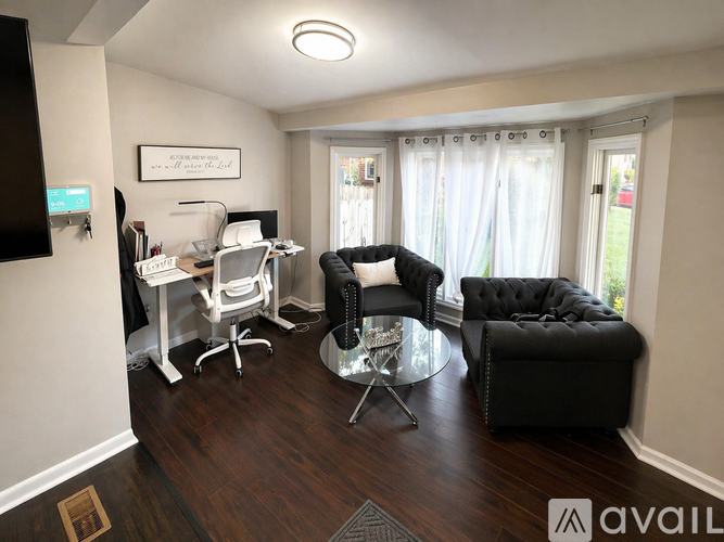 A living room with a black couch, a white desk, and a glass table.
