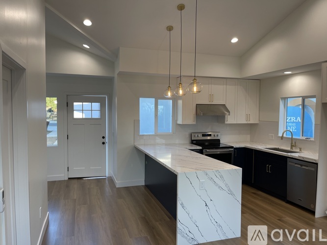A modern kitchen with a marble island and pendant lights.