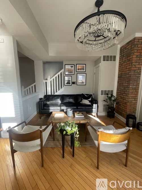 A living room with a black couch, wooden chairs, and a chandelier.