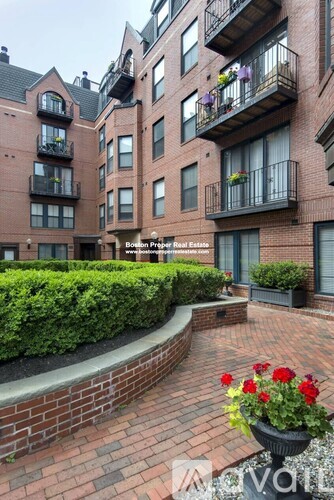 A brick building with balconies and a garden in front.