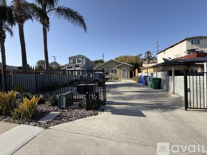 A sunny day in a residential area with houses, palm trees, and a black fence.