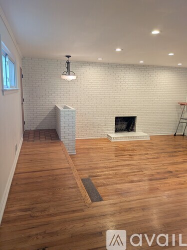 A room with wooden floors and a white brick wall with a fireplace.
