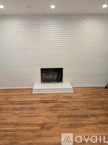 A white brick wall with a fireplace in the middle of a wooden floor.